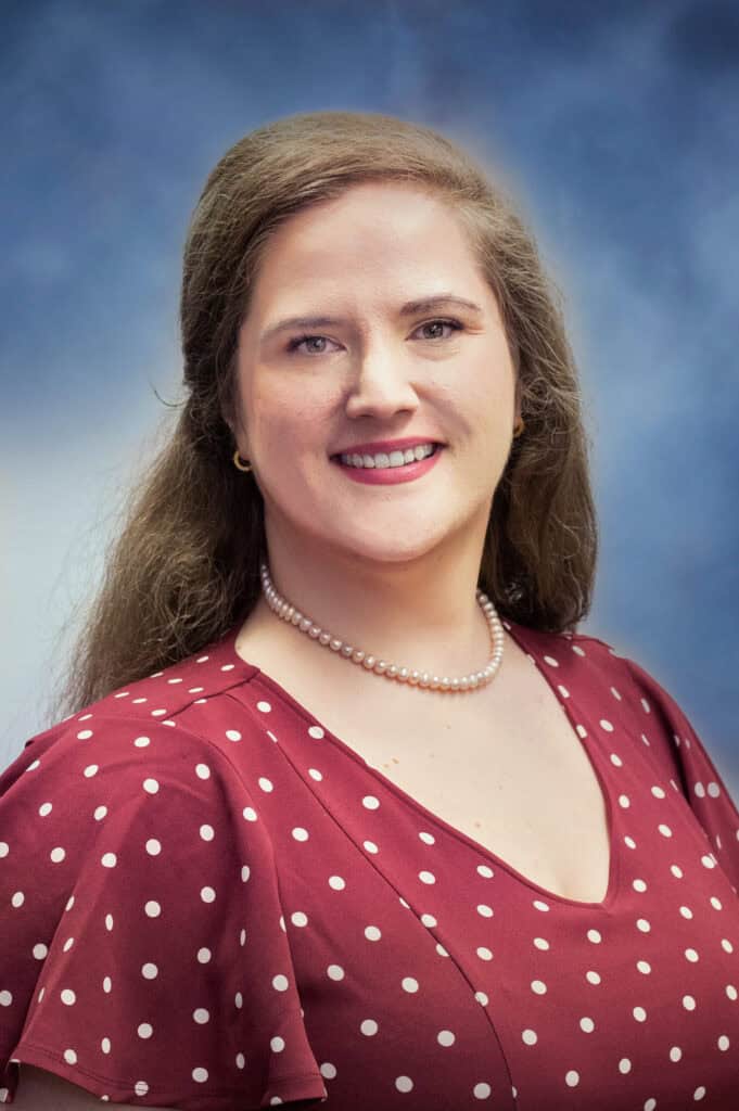 Dr. Laura Scott, MD, smiles at the camera with her long brown hair cascading over a maroon blouse adorned with white polka dots and a pearl necklace. The background features a soothing gradient of blue and white.